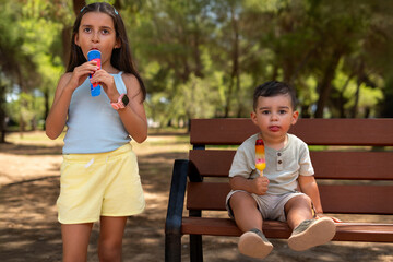 Two siblings enjoying refreshing ice cream while sitting on a park bench during a hot summer day