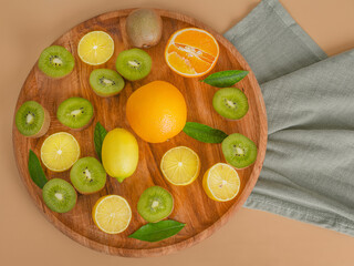 Citrus fruits lemons, orange and ripe kiwi on a wooden board on a beige background.