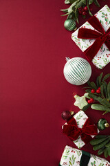 Stylish Christmas vertical background with gift box, balls, Xmas decorations, branches with berries on red table. Elegant, chic style.
