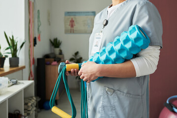 Medical professional holding blue foam roller and resistance bands while standing inside medical...