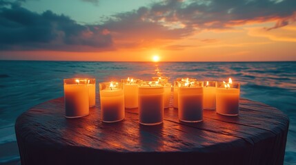 A row of candles lit on a wooden table on a beach at sunset.