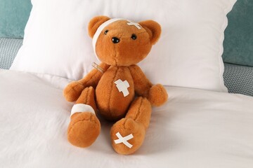Cute teddy bear with bandages, adhesive medical plasters and thermometer on bed