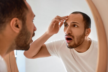Obraz premium Worried man looking at mirror in bathroom