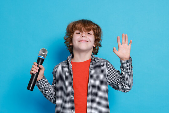 Little boy with microphone pretending to be singer on light blue background. Dreaming about future profession