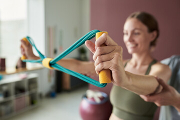 Woman smiling while using resistance bands during workout in fitness studio with blurred background of exercise equipment and natural light creating a serene atmosphere