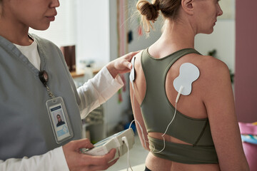 Healthcare professional using TENS unit on patient's back during physical therapy session....