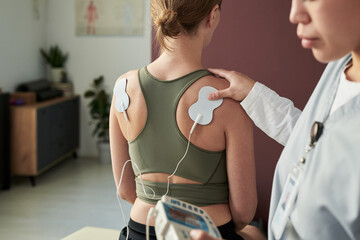 Woman experiencing therapeutic session with electrodes on back monitored by professional using...