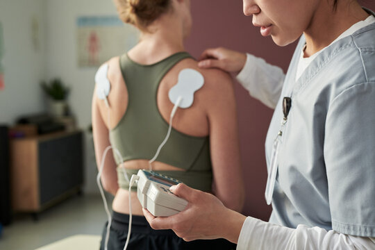 Physiotherapist conducting physical therapy session with patient using electronic device for muscle stimulation in medical setting
