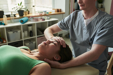 Fototapeta premium Massage therapist providing professional relaxation therapy in clinic setting. Client lying on massage bed while therapist attending soothing massage techniques for relaxation