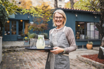 Obraz premium Smile woman waitress serving lemonade at restaurant garden