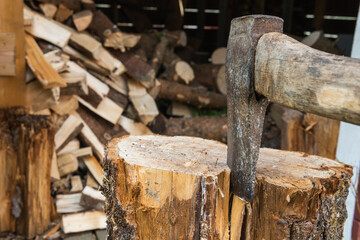 Close up photo of an Axe chopping up firewood. Wood logs in the background. Axe sitting in a log.