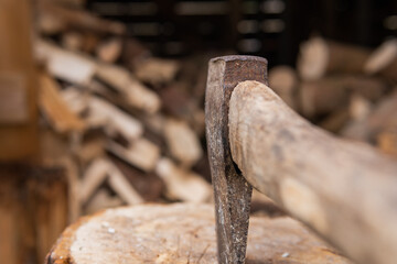 Close up photo of an Axe chopping up firewood. Wood logs in the background. Axe sitting in a log.