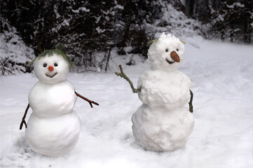 Young and old snowman in a winter forest with snowfall, New Year's scene.