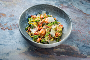 Traditional Italian Pasta with green Green asparagus, prawns and smoked salmon slices served with pine nuts and parmesan cheese slices as close-up in a Nordic design bowl