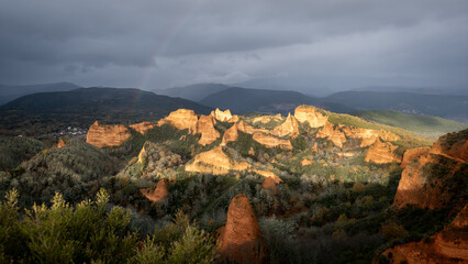 Fototapeta premium Las médulas ancient roman gold mines shining under cloudy sky and a rainbow at sunrise