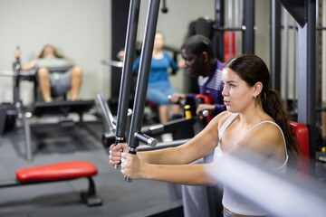 Sporty woman works on special simulator for the development of pectoral muscles