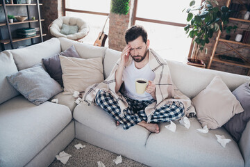 Photo of young ill man wearing pajama feeling unwell flu influenza sitting on sofa living room...