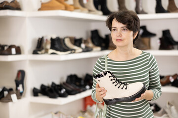 While shopping, woman takes samples from showcase and examines shoes. Client thinks about it and makes purchase decision, inquires about price.