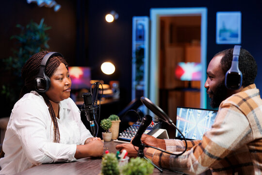 Black female presenter creates podcast with guest utilizing audio recording equipment in home studio. Young content creators chatting live during broadcasting session for an internet program.