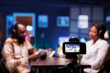 African American male and female bloggers recording podcast in studio with neon lights, filming a...