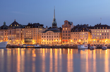 Fototapeta premium Scenic view of Stockholm waterfront at dusk showing illuminated historic buildings and the spire of Storkyrkan church, Stockholm, Sweden