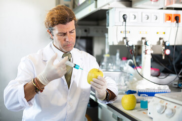 Adult male scientist chemist focused making injection of vaccine to yellow apple in laboratory