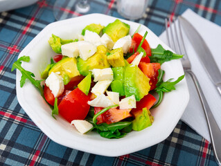 Healthy salad soft cheese, ripe avocado,tomatoes and arugula on whiteplate