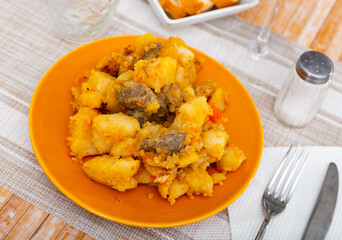 Fresh portion of braised potatoes with beef served on circular plate with serving pieces.