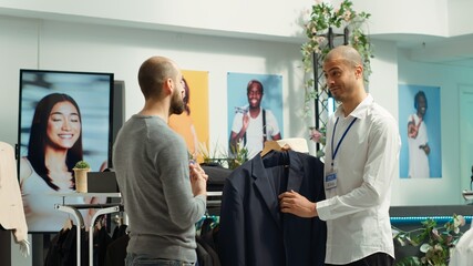 Obraz premium Middle eastern employee assisting client to choose from the new collection of items, presenting higher fabric quality and potential color assortments. Professional retail experience. Camera A.