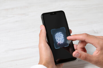 Man unlocking smartphone with fingerprint scanner at white wooden table, closeup