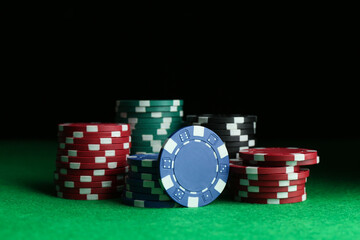 Poker chips on green table against dark background, closeup