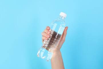 Woman holding plastic bottle of water on light blue background, closeup