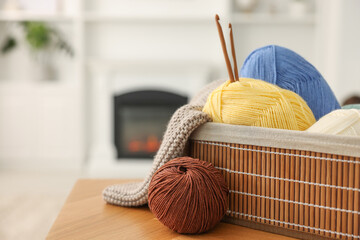 Colorful yarns, knitting sample, crochet hooks and basket on wooden table indoors, closeup. Space...