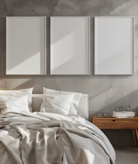Three blank picture frames hang above a bed with white linens against a concrete wall