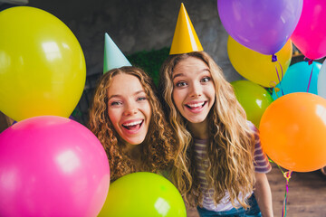 Two young women celebrating together with colorful balloons and party hats in a joyful living room...