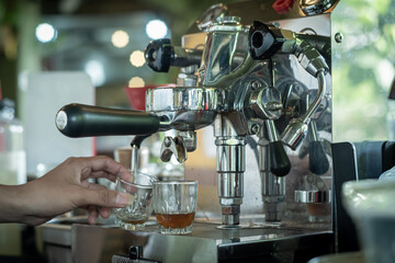 A barista who is making coffee and cappuccino drinks using a cappuccino machine on orders from customers in a cafe