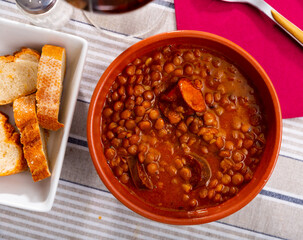 Traditional Spanish stewed lentils with meat, spicy chorizo sausages and vegetables in gravy served in clay cazuela