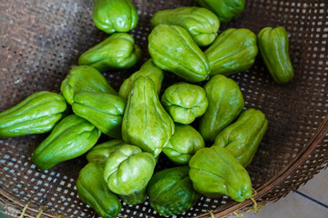 A wicker basket overflowing with freshly harvested chayotes. Vibrant green chayotes ready for cooking or market. A Bountiful Basket of Fresh Green Chayotes