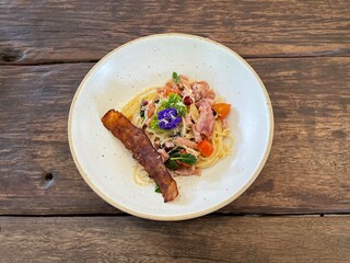 Spicy and herbs spaghetti with hams and beacons in white ceramic dishes on wooden table