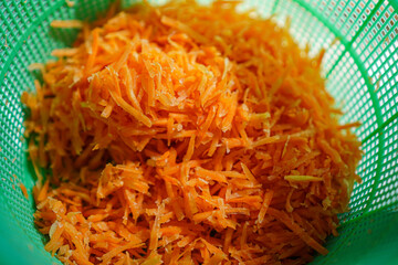A detailed view of freshly shredded carrots piled high in a bright green colander. Close-up of Shredded Carrots in a Green Colander for Food Preparation.