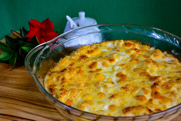 A delicious cauliflower gratin, baked golden with melted cheese on top. The dish is served on a white plate with a garnish of herbs, set on a wooden table in a cozy kitchen.