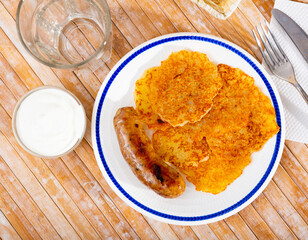 Fried grated potato pancakes with sour cream and sausage closeup. Belorussian cuisine