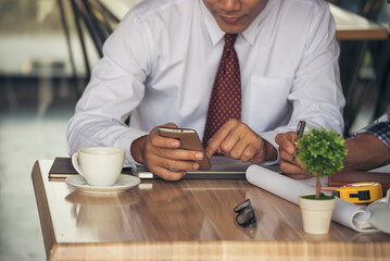 Business colleague working together using smartphone searching website and blogs for business news in conference room. Asian young man wear suit and tide formal dress waiting meeting. Business concept