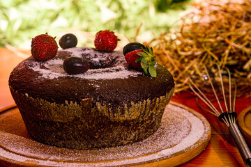 A close-up shot of a beautifully decorated chocolate cake with intricate piping and chocolate shavings on top. The cake is set on a rustic wooden table with soft lighting.