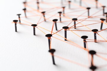Network connection. Nails linked together by thread on white table, closeup
