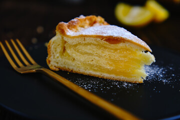 Lemon pie on a black plate with aromatic coffee on an old wooden table
