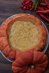 A delicious Brazilian dish featuring shrimp in a pumpkin (camarão na moranga), garnished with fresh biquinho and dedo de moça peppers, set on a wooden background. Vibrant and flavorful.
