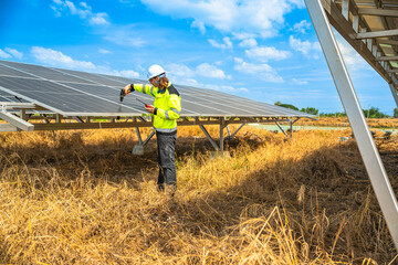An engineer wearing safety gear inspects a large solar panel using a power drill under a vibrant...