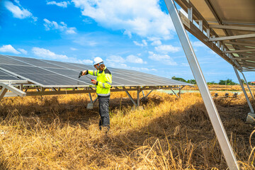 An engineer wearing safety gear inspects a large solar panel using a power drill under a vibrant...