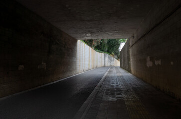 Dark urban underpass or tunnel with a narrow pedestrian pathway alongside a roadway leads towards a...